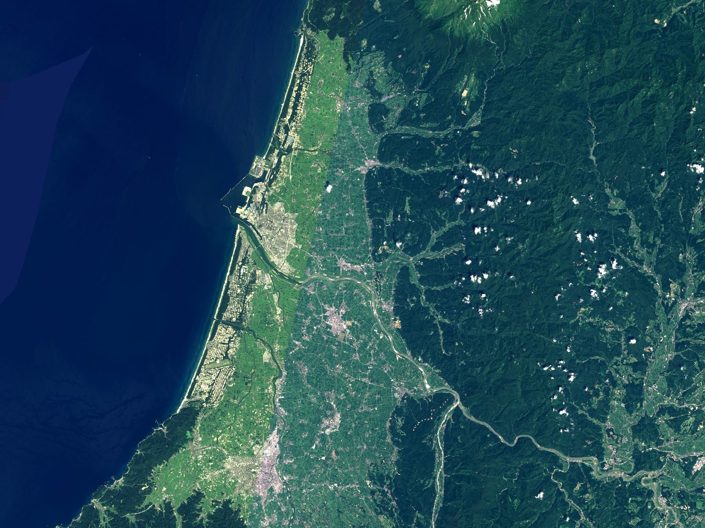 宇宙から見た庄内平野。左に日本海、まん中に緑の平野、右に山地が広がり、平野を川が横切って海に流れこんでいる