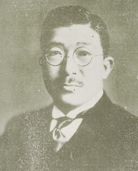 丸いめがねをかけ、口ひげをはやした、スーツの男性
