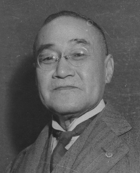 めがねをかけ、スーツにネクタイをしめた年配の男性
