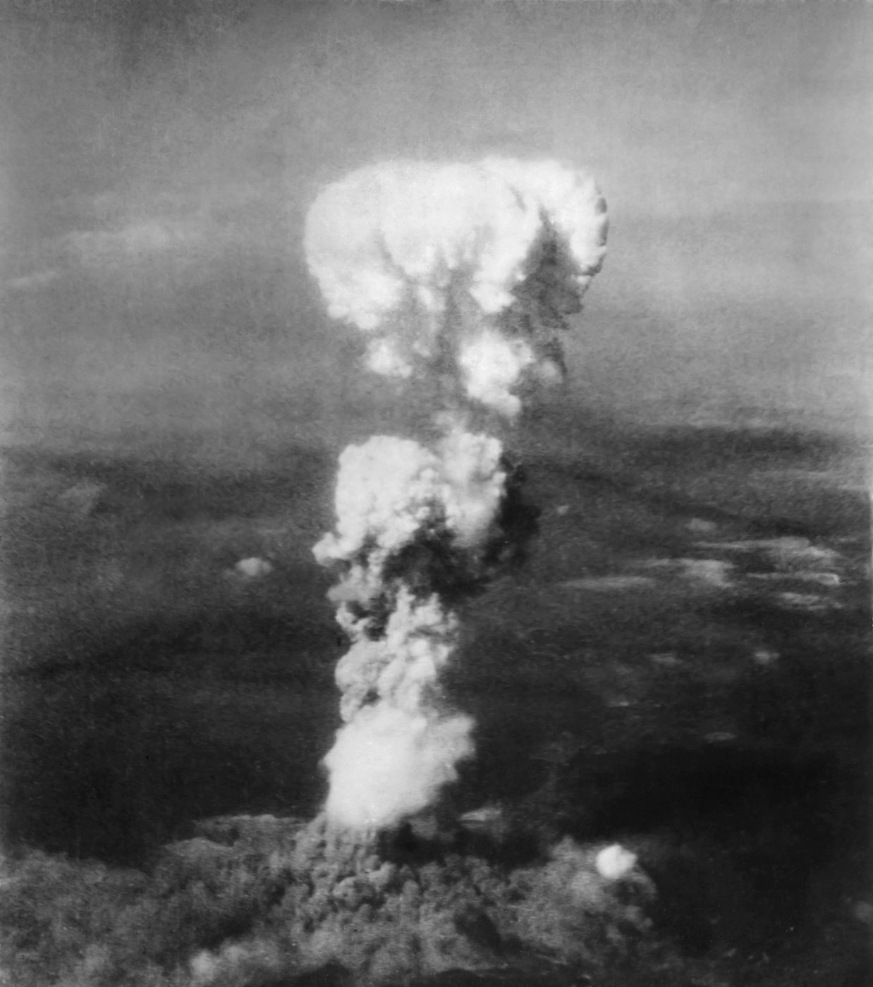 雲の上の空に、白いけむりが柱のように高く立ちのぼり、上が大きく広がっている白黒の写真