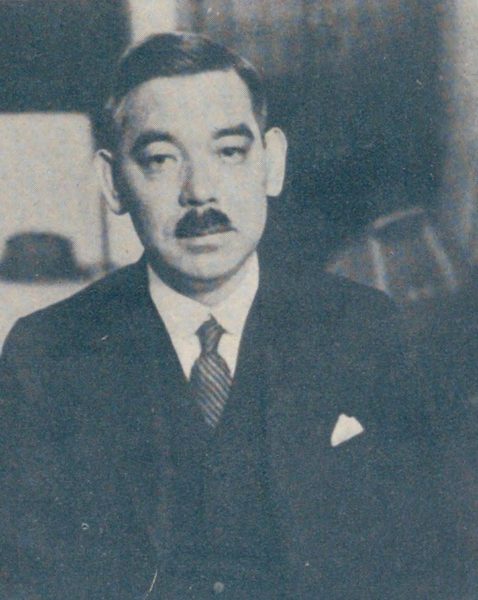 口ひげをはやし、スーツにネクタイの男性