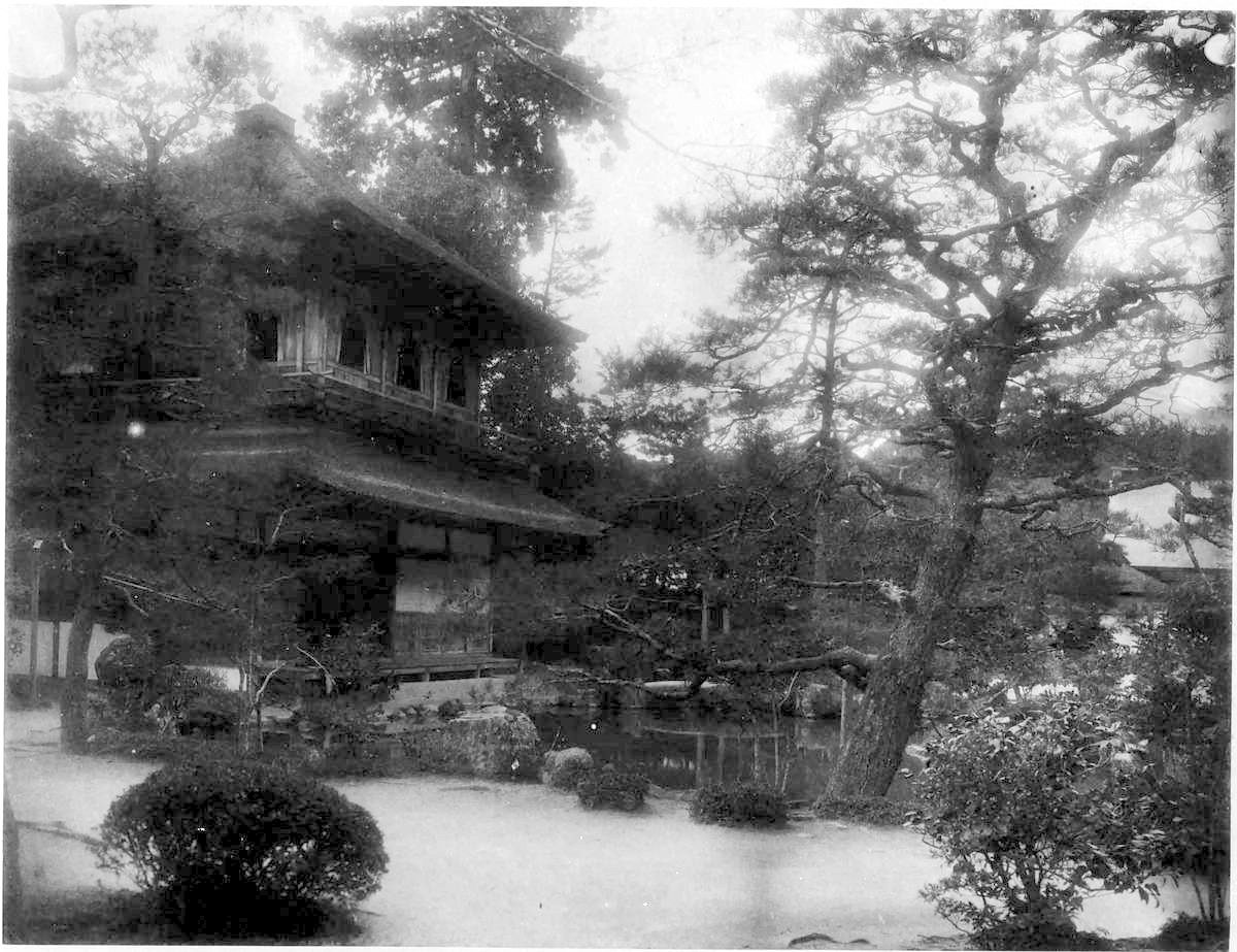 松の木と庭の池のそばに建つ、屋根のある2階建ての建物の古い白黒写真