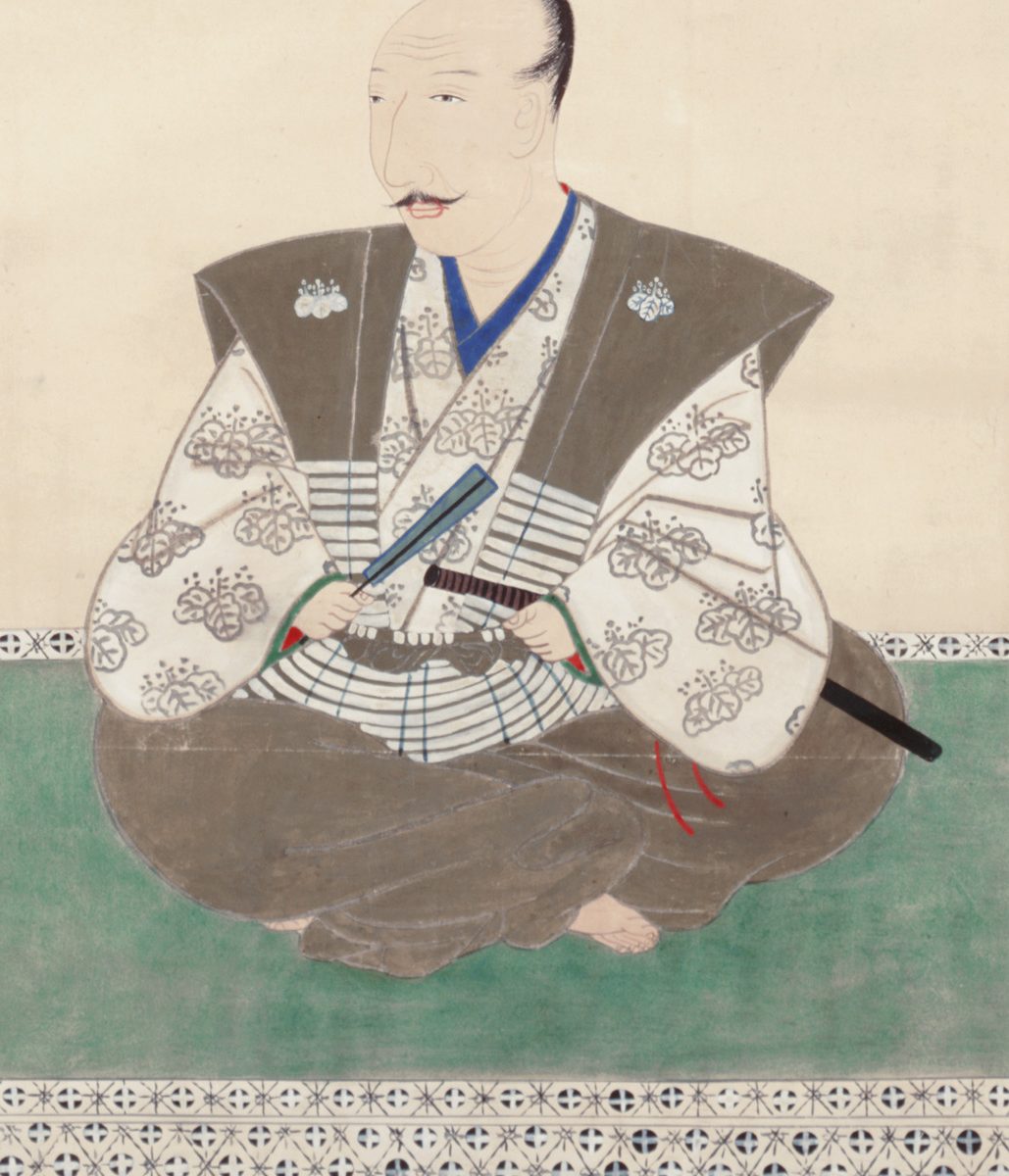 白い着物と茶色い上着を着て、あぐらをかいて座る、口ひげのある男性の肖像画。手に扇と刀をもっている