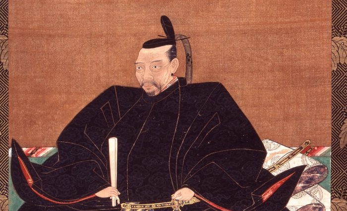 黒い着物すがたで、笏と太刀を持って座る、ひげのある男性の肖像画