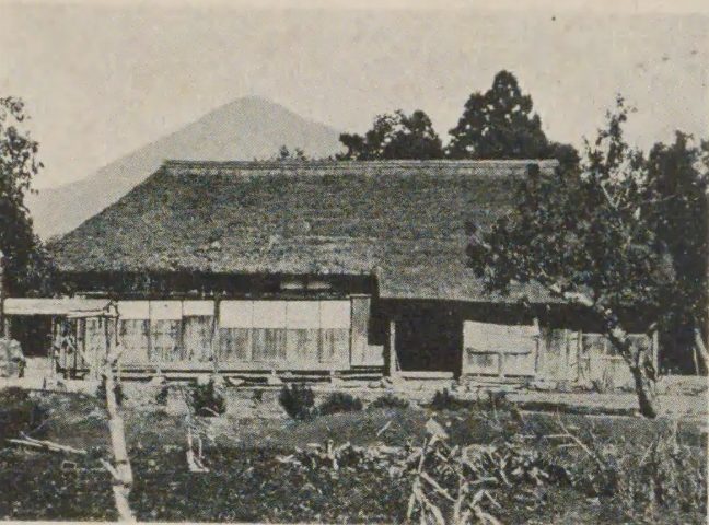 かやぶき屋根の古い農家と、そのうしろにそびえる山の写真