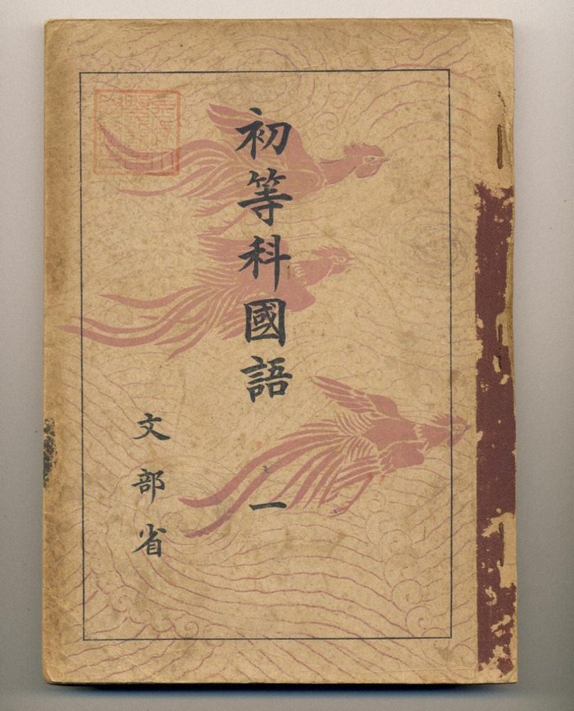うすいピンクの鳥の模様の表紙に「初等科國語 一」「文部省」と書かれた教科書