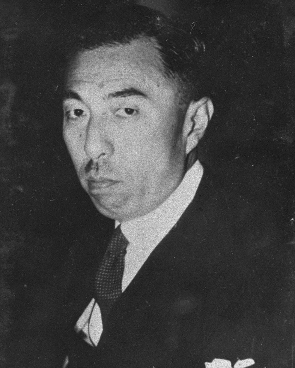 髪をなでつけ、口ひげをはやした、スーツにネクタイの男性